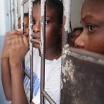 Three children looking outside from behind bars